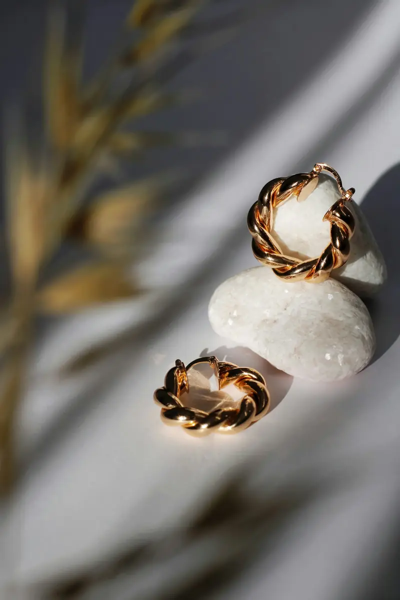 Gold earrings displayed on a stone in soft studio light