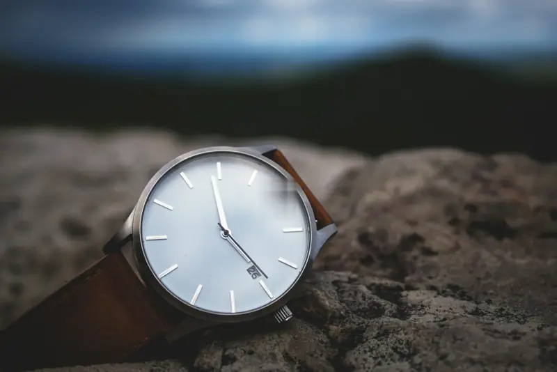 Steel date watch with silver-white dial and tan leather strap on stone
