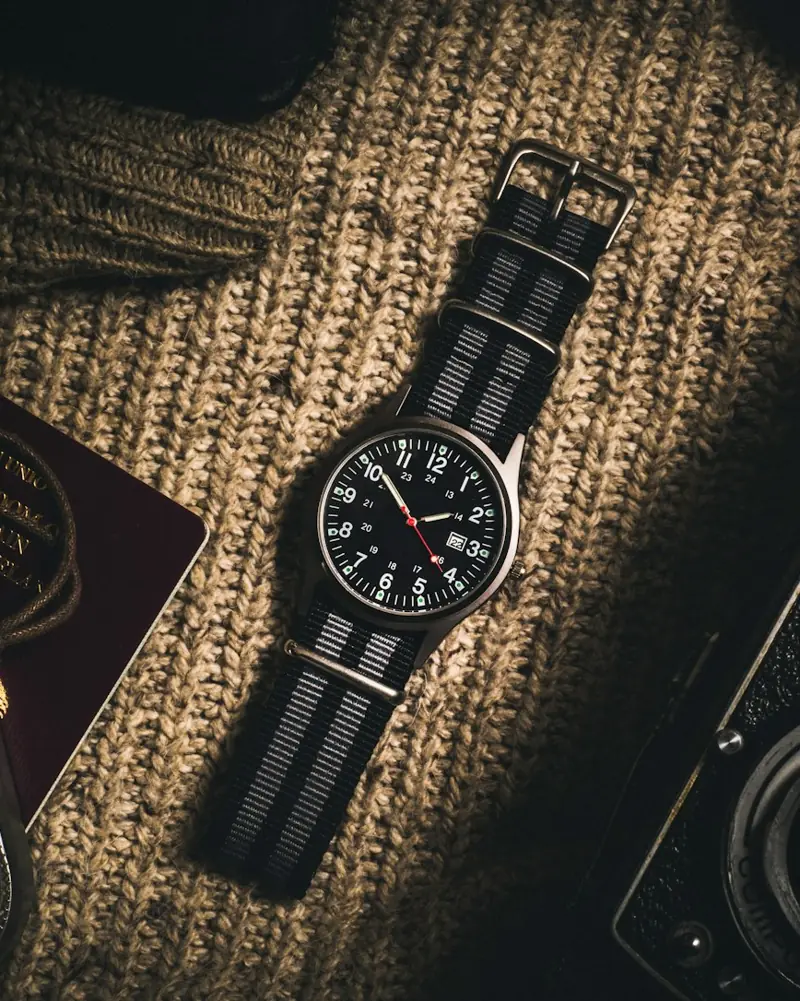 Atelier Field watch with black dial on a striped strap over wool knit